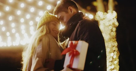 Happy couple stand hugging outdoors. Boyfriend making holiday surprise to his woman celebrating together giving christmas present. Gift box. Slow motion - Powered by Adobe