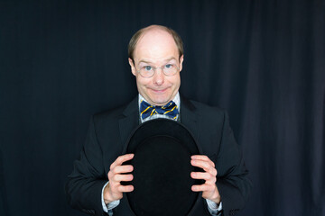 Portrait of Man in Dark Suit and Bow Tie Holding Bowler Hat and Smiling Nervously. Concept of...