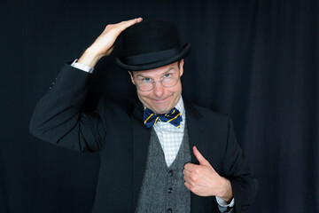 Portrait of Man in Dark Suit and Patting His Bowler Hat. Concept of Classic and Eccentric English Gentleman.