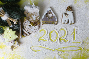 gingerbread covered with royal icing in the form of a house, deer and Christmas tree baked for Christmas and numbers 2021 on a background of sifted flour
