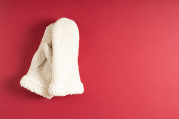 Winter background. White warm knitted mittens on red background. Flat lay, top view, copy space