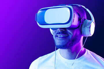 Afro american man wearing VR glasses in neon light against purple background