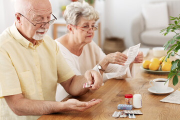Senior couple sitting at dining table taking medicines