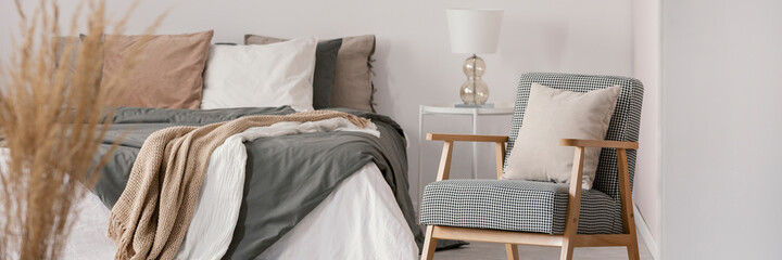 Retro armchair next to a comfy bed in a natural bedroom interior. Real photo