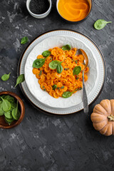Pumpkin pasta with spinach in a white plate on a dark gray table. Dinner. Flat lay.