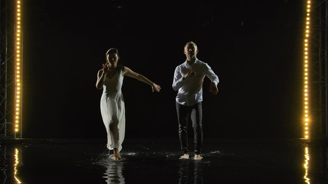 A couple dancing salsa in white. Passionate hot beautiful dance performed in a dark studio on a water surface with many splashes. Slow motion.