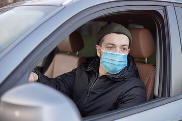 Man driving a car wearing on a medical mask during an epidemic. Young male driver inside car with protective face mask.