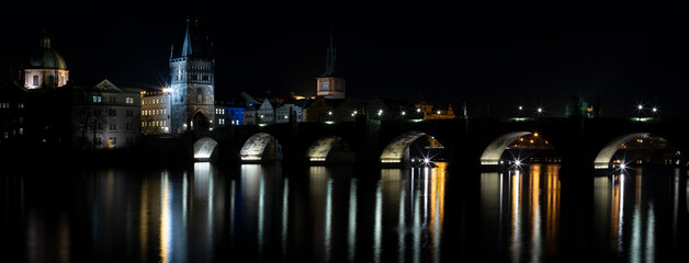 
illuminated Charles Bridge from 14 centuries and light from street lighting and stone sculptures on the bridge and light reflections on the surface of the Vltava river at night in Prague