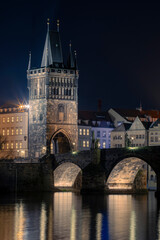 
illuminated Charles Bridge from 14 centuries and light from street lighting and stone sculptures on the bridge and light reflections on the surface of the Vltava river at night in Prague