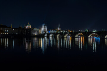 Fototapeta premium illuminated Charles Bridge from 14 centuries and light from street lighting and stone sculptures on the bridge and light reflections on the surface of the Vltava river at night in Prague