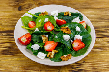 Fresh healthy salad with strawberry, spinach, walnuts and feta cheese on wooden table