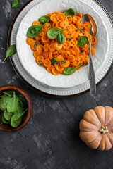 Pumpkin pasta with spinach in a white plate on a dark gray table. Dinner. Flat lay.