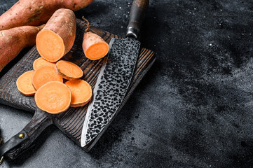 Raw cut batata Sweet potato on Wooden cutting board. Black background. Top view. Copy space