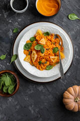 Pumpkin pasta with spinach in a white plate on a dark gray table. Dinner. Flat lay.