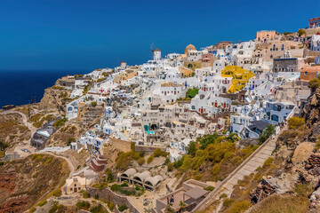 Fototapeta na wymiar The white buildings of the village of Oia, Santorini tumble down the cliff towards Amoudi Bay in summertime