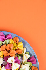Grey plate and colorful farfalle pasta on a orange flat lay. Food ingredients background. Italian concept. Top view.