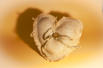 Brown fabric heart with button and cord on golden background.