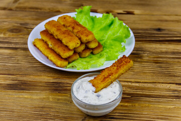 Fried fish fingers on a plate with lettuce and tartar sauce on wooden table