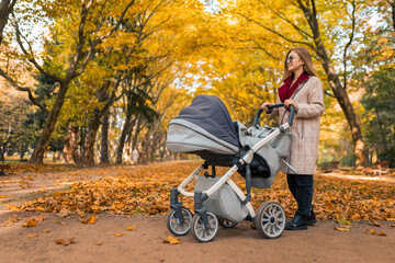 Stylishly dressed mom with stroller in autumn park