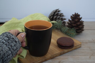 hand holds a cup of tea and cookies on the background of fir branches and cones