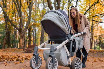 Fototapeta na wymiar Cheerful mom playing with newborn baby in stroller. Woman walking in the park with pram