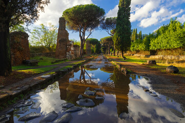 Beautiful moment in the Appian Way after the storm, reflects the ruins of the tree graves in the puddle with the blue of the sky and clouds on an autumn day. Regina Viarum, Rome Italy.