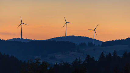 three wind turbines in the mountains at sunset
