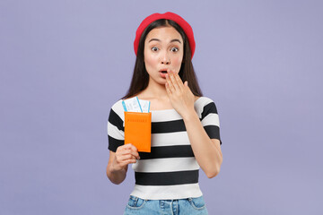 Shocked asian woman in striped t-shirt red beret hold passport ticket covering mouth with hand isolated on violet background. Passenger traveling abroad on weekend getaway. Air flight journey concept.