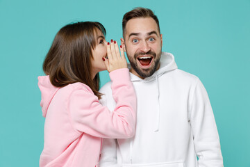 Excited young couple two friends man woman 20s wearing white pink casual hoodie standing whispering...