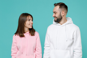 Smiling cheerful funny young couple two friends man woman 20s wearing white pink casual hoodie standing looking at each other isolated on blue turquoise colour wall background studio portrait.