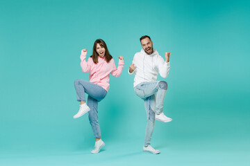 Fototapeta na wymiar Full length of overjoyed screaming young couple two friends man woman 20s in white pink casual hoodie doing winner gesture clenching fists isolated on blue turquoise wall background studio portrait.