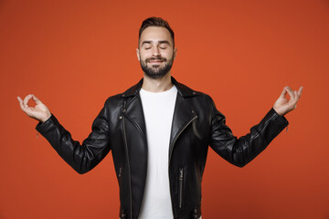 Smiling young bearded man 20s in white t-shirt, black leather jacket hold hands in yoga gesture, relaxing meditating, trying to calm down isolated on bright orange colour background, studio portrait.