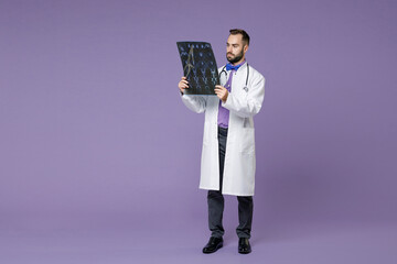 Full length of young bearded doctor man in medical gown hold x-ray brain by radiographic image ct scan mri isolated on violet background studio portrait. Healthcare personnel health medicine concept.