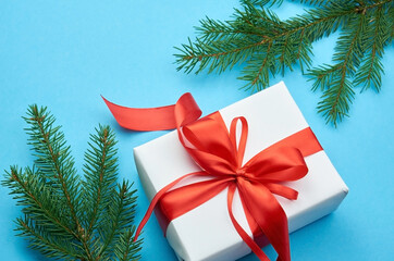 White gift box with red ribbon bow with fir tree branches on blue background