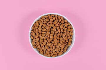 Bowl with dry kibble cat or dog food on pink background