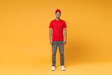 Full length delivery employee african man 20s in red cap blank print t-shirt uniform workwear work courier dealer service during quarantine covid-19 virus concept isolated on yellow background studio.