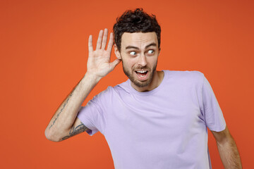 Shocked curious young bearded man 20s wearing basic casual violet t-shirt standing try to hear you...