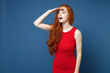 Shocked amazed young redhead woman 20s wearing bright red elegant evening dress standing holding...