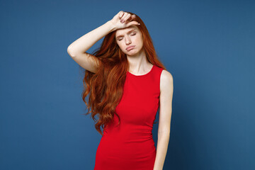 Exhausted tired dissatisfied young redhead woman 20s wearing bright red elegant evening dress standing put hand on head keeping eyes closed isolated on blue color wall background studio portrait.