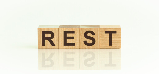 Wooden Blocks with the text: rest. The text is written in black letters and is reflected in the mirror surface of the table.