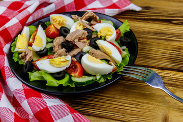 Tasty tuna salad with lettuce, black olives, eggs and fresh vegetables on wooden table