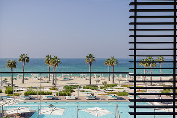 Fototapeta na wymiar Wonderful balcony view on a seashore and a pool with palm trees on a sunny day