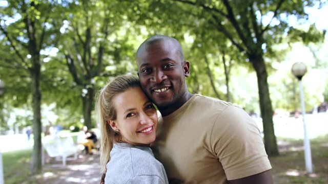 Multiracial couple hugging in public park.