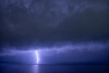 Single linear lightning over the sea with reflection under dark clouds