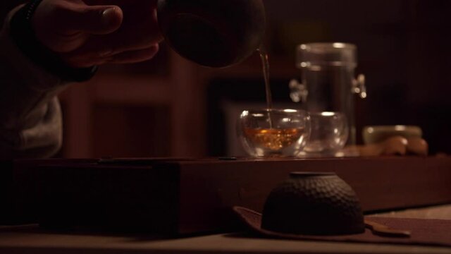 Close-up of the hand of an Asian master pouring tea into cups standing on the chaban, from a real teapot made of yixing clay.
