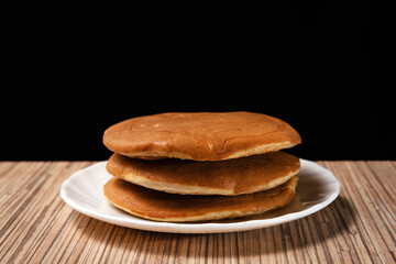 Stack of 3 pancakes on white plate with a dark background 