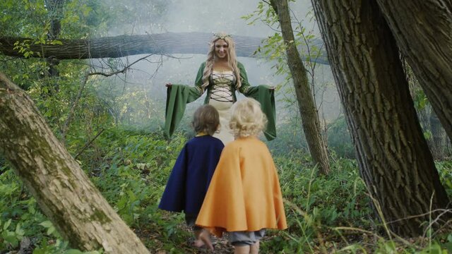 Scene of meeting elf woman and little hobbits or gnome toddler boys in green forest. Cosplay, halloween, fairy tale characters concept.