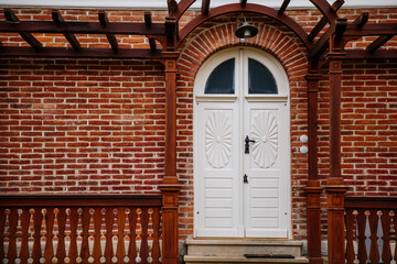 Classic wooden white carved oval door with glass inserts, brown canopy and lamp over porch, red block brick wall, entrance to residential apartment, Veltrusy castle, Czech republic