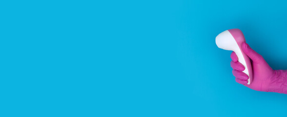 Hand in pink medical glove holds pyrometer on blue background with copy space.