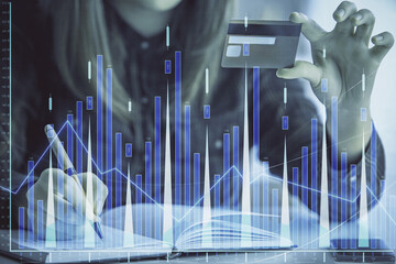 Double exposure of woman on-line shopping holding a credit card and financial graph drawing. Stock market E-commerce concept.
